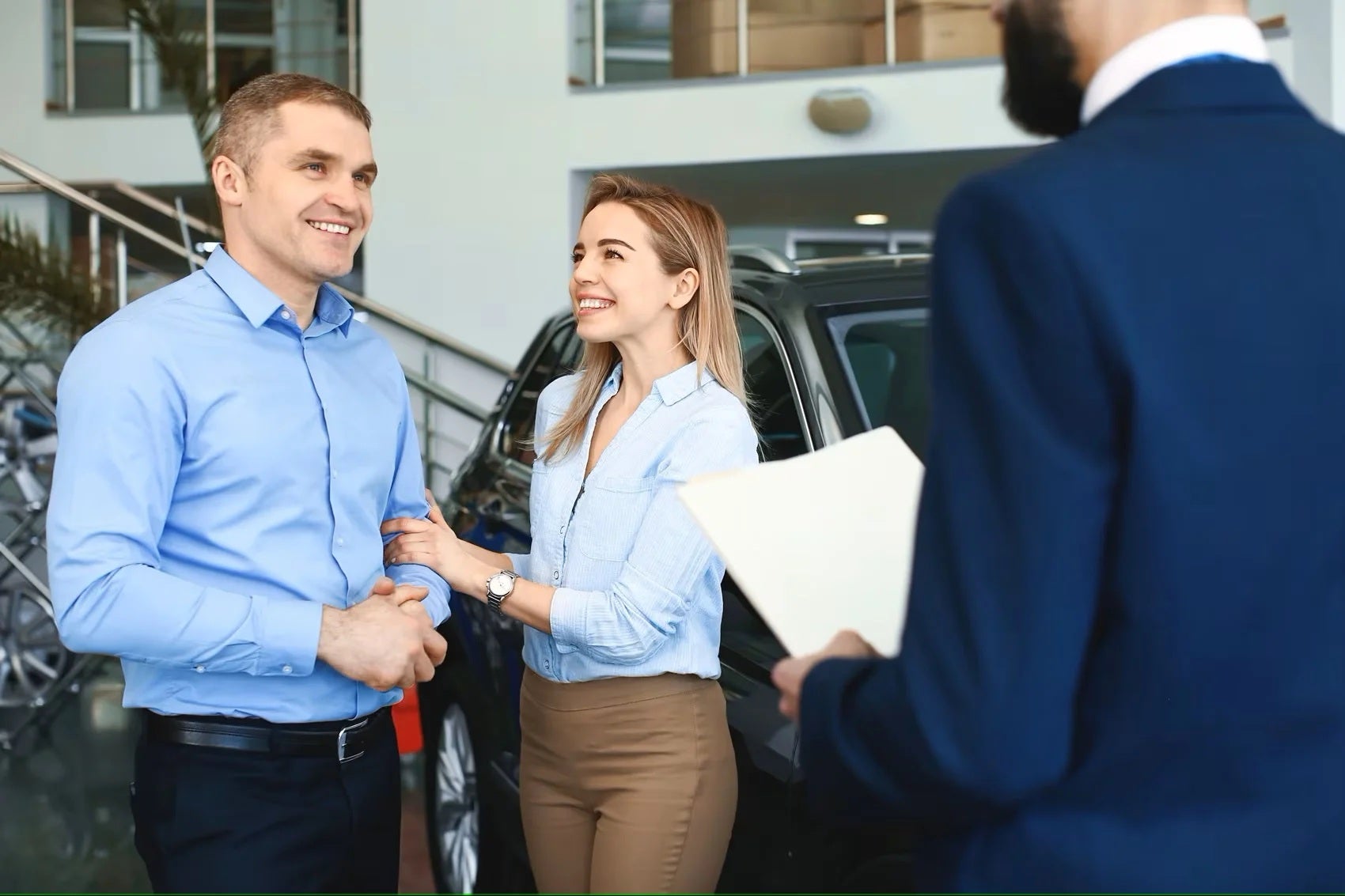 Happy couple next to new car in dealer showroom